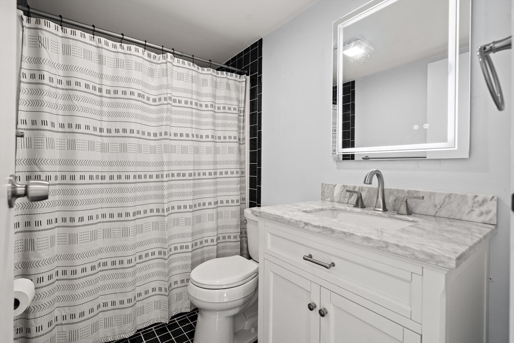 159 Franklin Street, Unit E6 Stoneham, MA 02180 - Photo 16 of 22 a bathroom with a granite countertop sink a toilet and a mirror