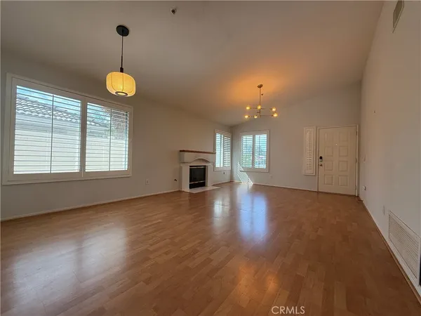 an empty room with wooden floor chandelier and windows