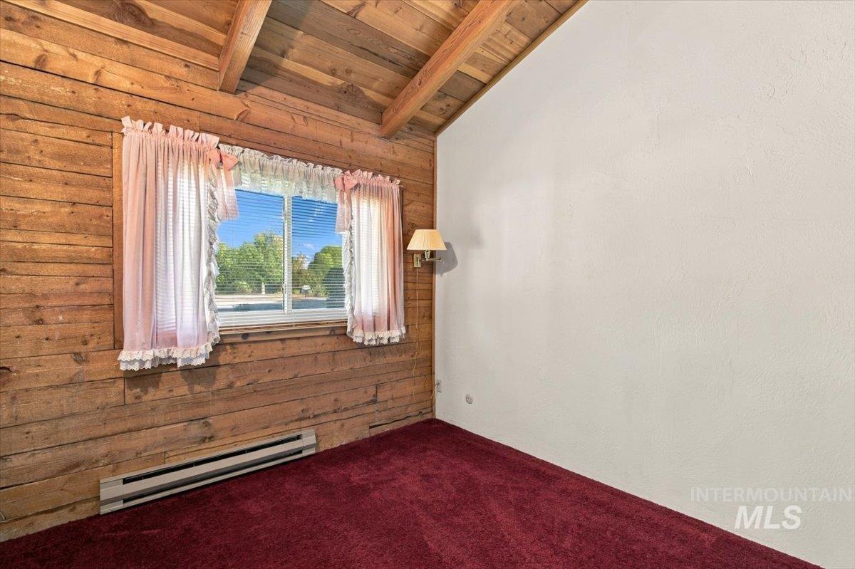 10201 Willis Road Middleton, ID 83644 - Photo 15 of 38 Wood-paneled wall with exposed beams, contrasting white wall, window with blinds, wall-mounted light fixture, and red carpeting