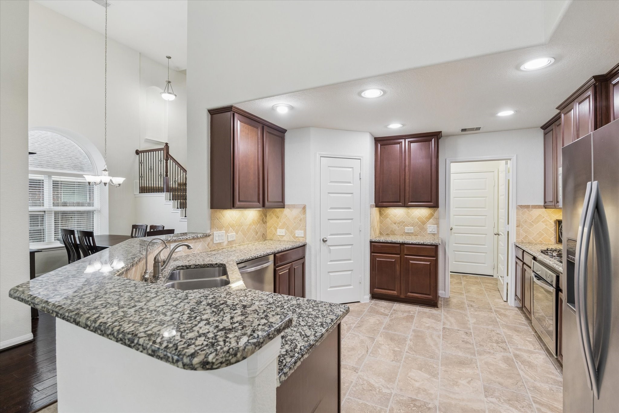7015 Riata Hills Lane Spring, TX 77379 - Photo 11 of 33 A beautifully appointed kitchen with granite countertops, elegant tile flooring, and LED lighting. The breakfast bar provides ideal seating for guests, complemented by a spacious walk-in pantry for added convenience.