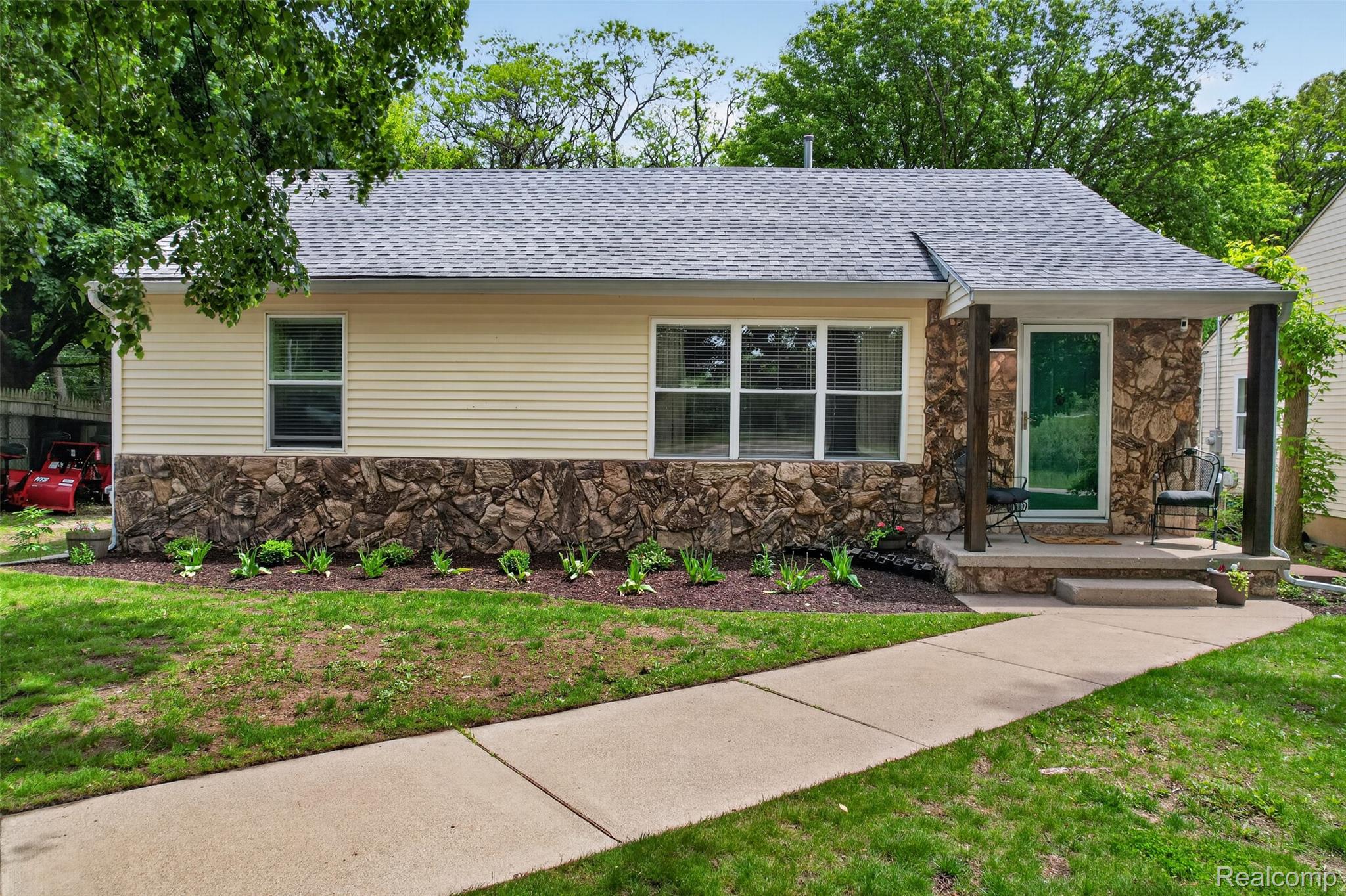 View of front of home featuring stone siding, a front yard, and roof with shingles