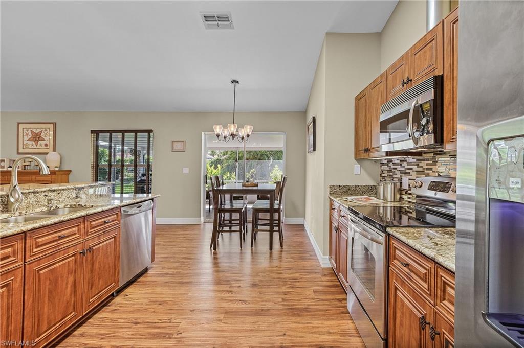 128 Plantation Circle Naples, FL 34104 - Photo 8 of 27 a kitchen with stainless steel appliances granite countertop a stove top oven a sink dishwasher a dining table and chairs with wooden floor