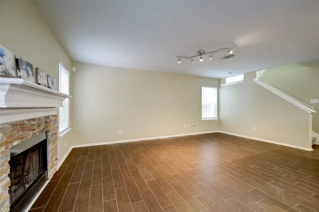 an empty room with wooden floor fireplace and windows