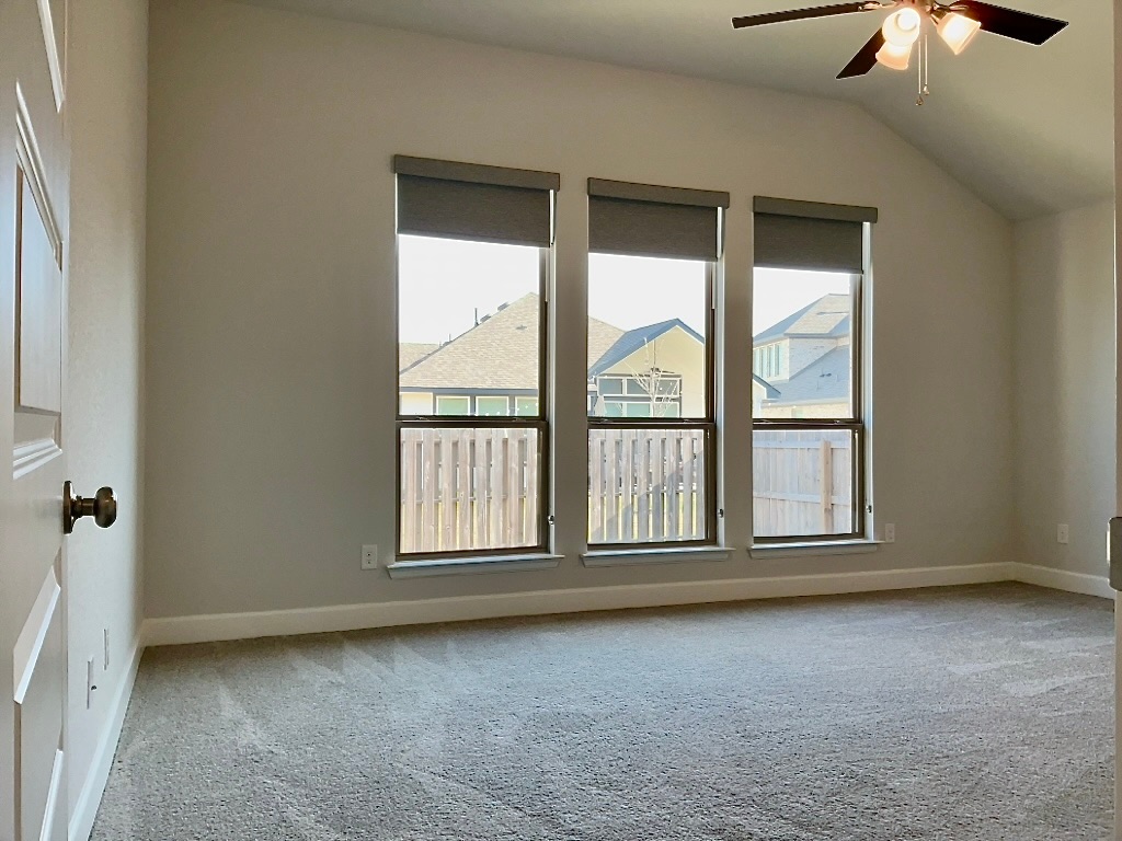 1636 Laverne Mitchell Street Leander, TX 78641 - Photo 9 of 20 Primary bedroom with ceiling fan, light carpet, lofted ceiling and wall of windows with view the th backyard.