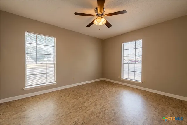 an empty room with chandelier fan and windows
