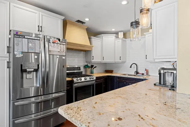 a kitchen with stainless steel appliances granite countertop a refrigerator a sink a stove and white cabinets