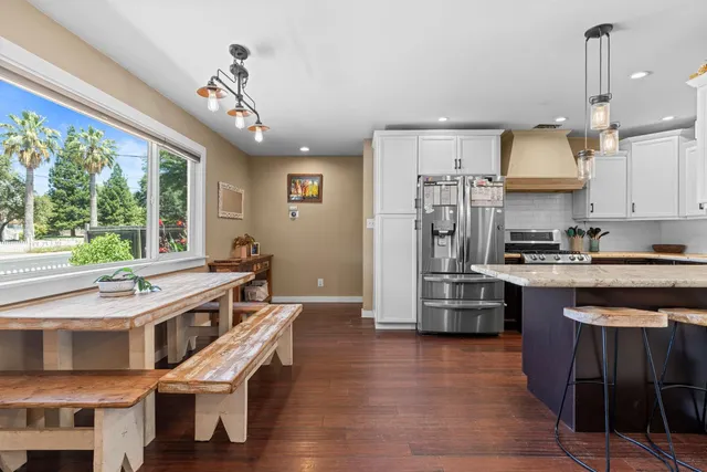 a kitchen with stainless steel appliances granite countertop a refrigerator a sink dishwasher a stove and a dining table with wooden floor