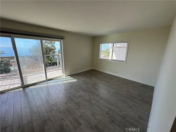 an empty room with wooden floor mirror and windows