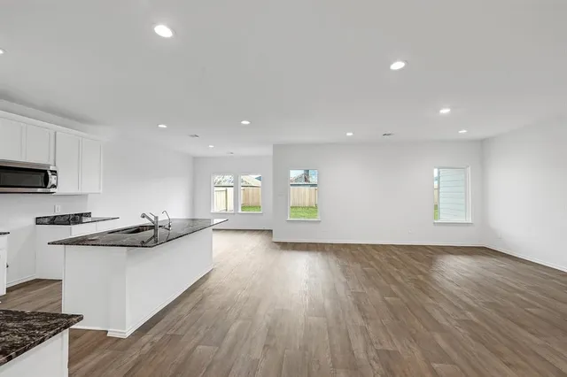 a kitchen with stainless steel appliances granite countertop a stove a sink a refrigerator a microwave a sink and white cabinets with wooden floor
