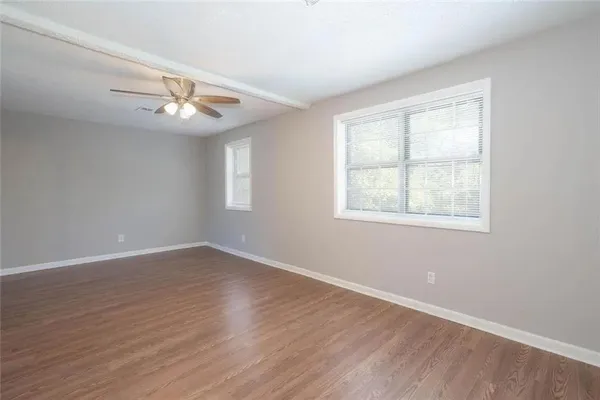 an empty room with wooden floor chandelier fan and windows