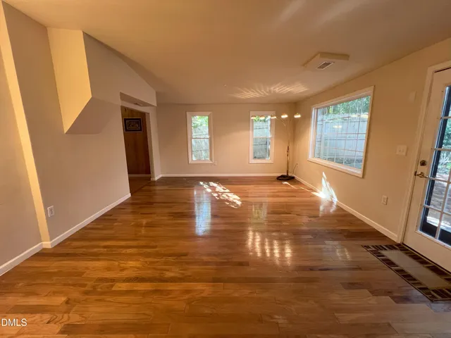 a view of an empty room with wooden floor and a window