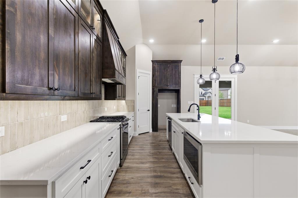 702 Anne Road Van Alstyne, TX 75495 - Photo 4 of 27 Kitchen featuring dark wood-finish upper cabinetry, white lower cabinetry, and an expansive white countertop island