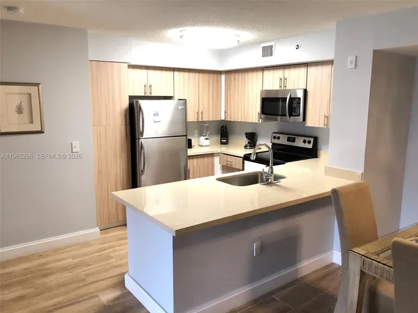 a kitchen with stainless steel appliances a sink a refrigerator a counter space and wooden floor