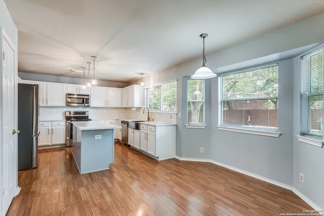 a kitchen with granite countertop a stove a sink dishwasher a refrigerator and white cabinets with wooden floor