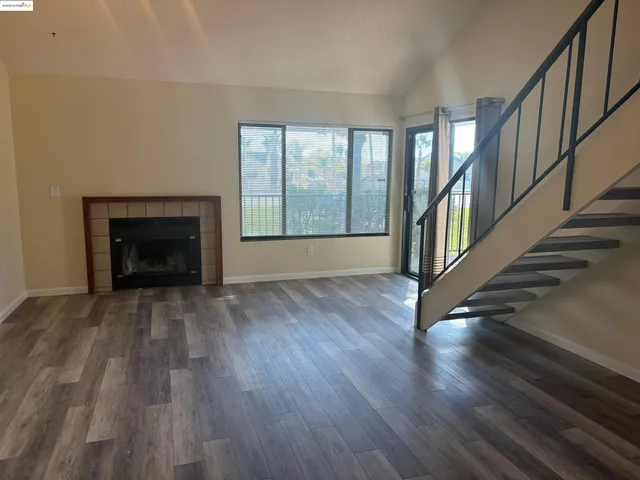 a view of an empty room with wooden floor fireplace and a window