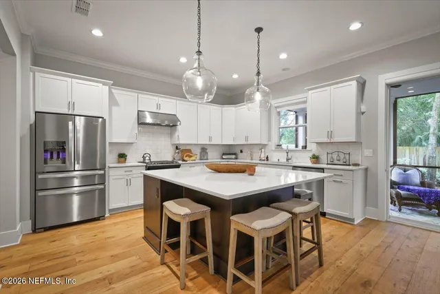 a kitchen with stainless steel appliances granite countertop a refrigerator a sink dishwasher a stove and white cabinets with wooden floor