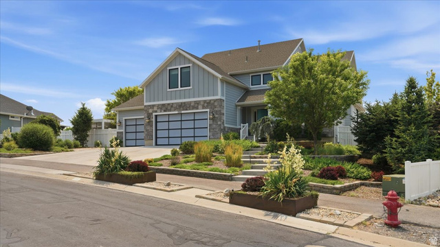 2038 East Ranch Road Eagle Mountain, UT 84005 - Photo 2 of 66 Contemporary residential exterior featuring light blue siding, stone accents, multiple gables, and a two-car garage with modern glass-paneled doors