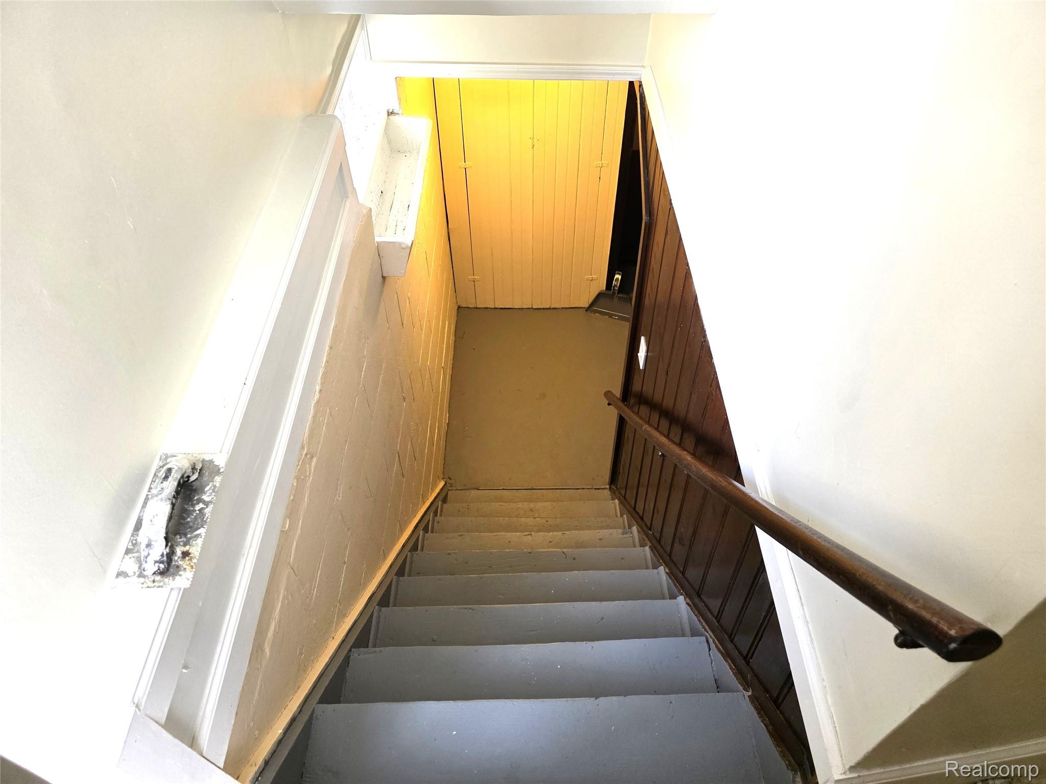16814 Strathmoor Street Detroit, MI 48235 - Photo 20 of 31 Stairwell featuring a wooden handrail, painted steps, white wall finishes, and wood paneling