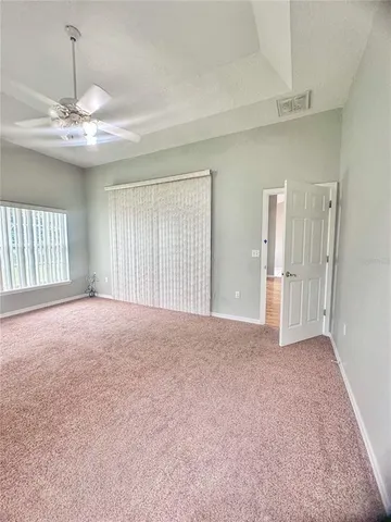 a view of an empty room with chandelier fan and windows
