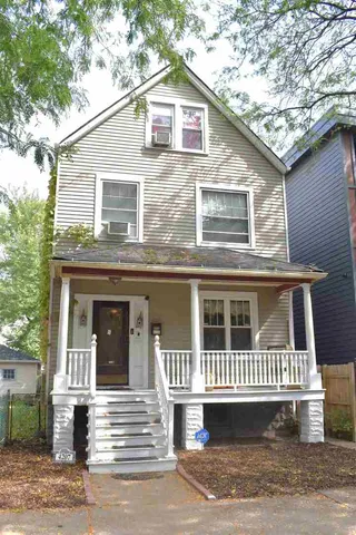 a view of a brick house with large windows and a yard with plants and large trees