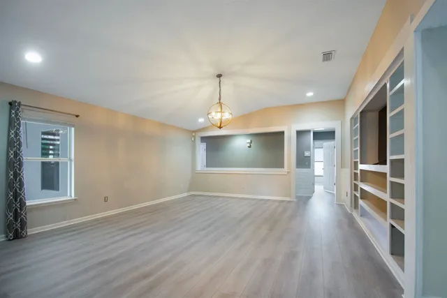 an empty room with wooden floor kitchen view and a window