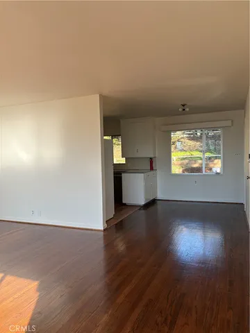 an empty room with wooden floor cabinet and windows