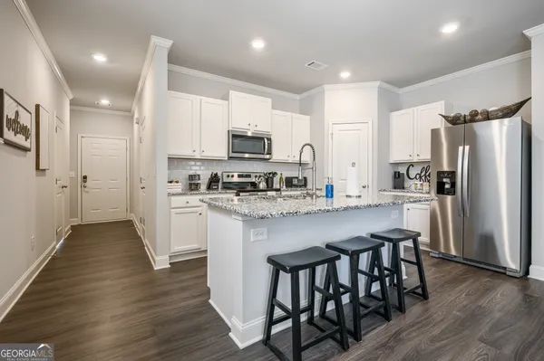 a kitchen with stainless steel appliances a refrigerator a stove a sink a white table and chairs with wooden floor