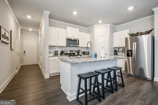 a kitchen with stainless steel appliances a refrigerator a stove a sink a white table and chairs with wooden floor