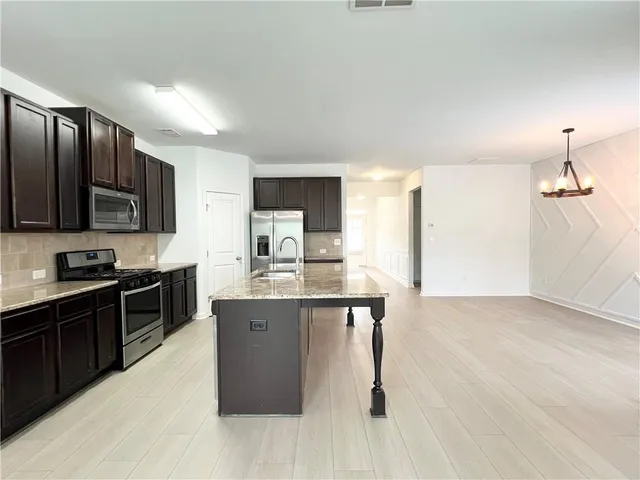 a kitchen with stainless steel appliances granite countertop a stove top oven a sink dishwasher a refrigerator and a dining table with wooden floor