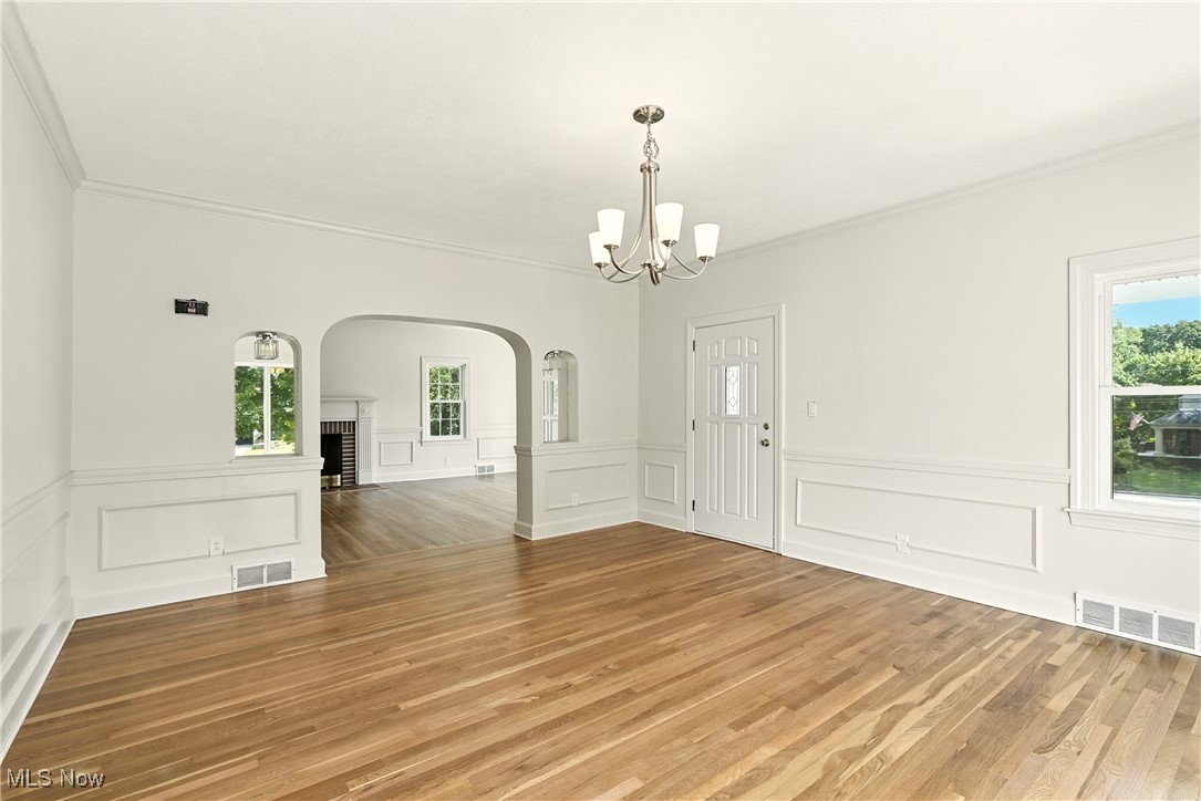Unfurnished dining area featuring a brick fireplace, light wood-type flooring, a chandelier, ornamental molding, and arched walkways