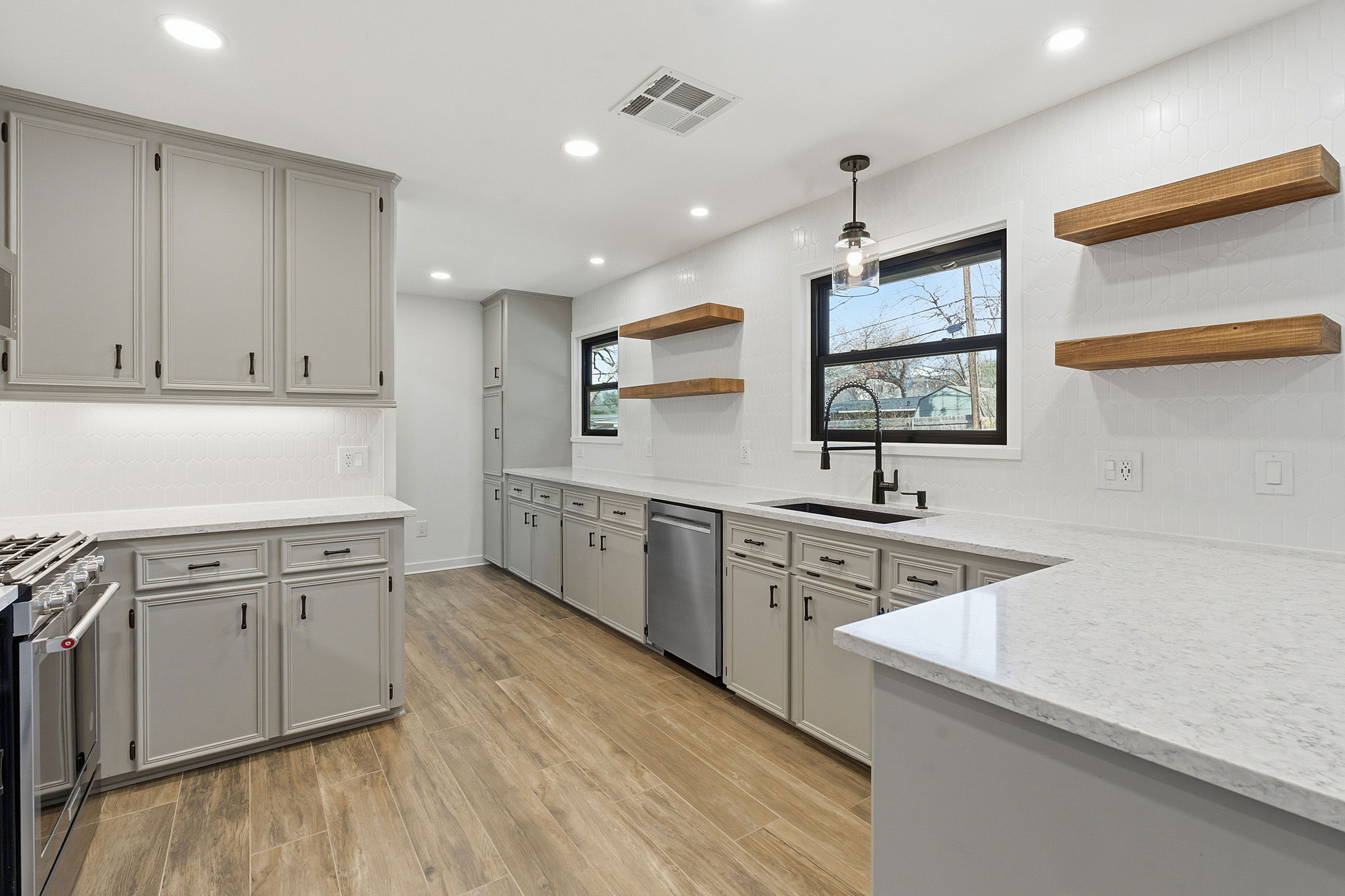 5609 Mapleleaf Drive Austin, TX 78723 - Photo 6 of 19 Kitchen featuring open shelves, light wood-type flooring, stainless steel appliances, hanging light fixtures, and light stone countertops