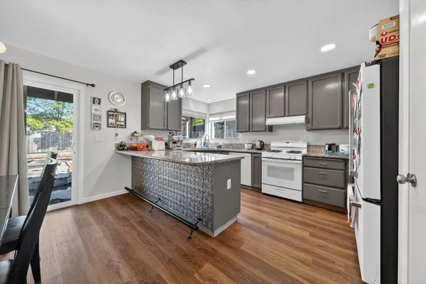 a kitchen with stainless steel appliances granite countertop a refrigerator a stove top oven a sink dishwasher and white cabinets with wooden floor