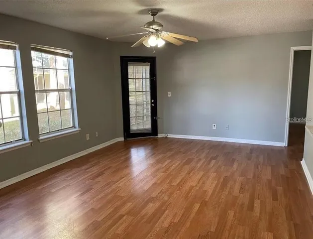 an empty room with wooden floor chandelier fan and windows