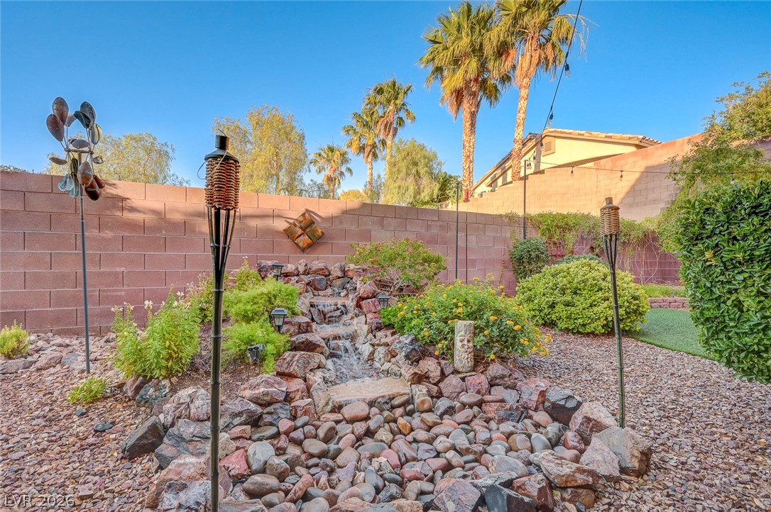1604 Cattle Ranch Place Henderson, NV 89002 - Photo 77 of 99 A tranquil backyard retreat features a rock-lined waterfall and mature landscaping for serene outdoor living.
