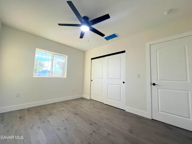 an empty room with wooden floor a ceiling fan and windows
