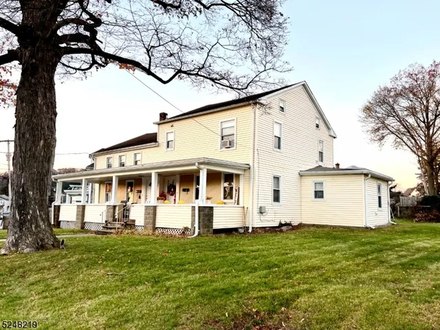 a view of a white house with a big yard with large tree and plants