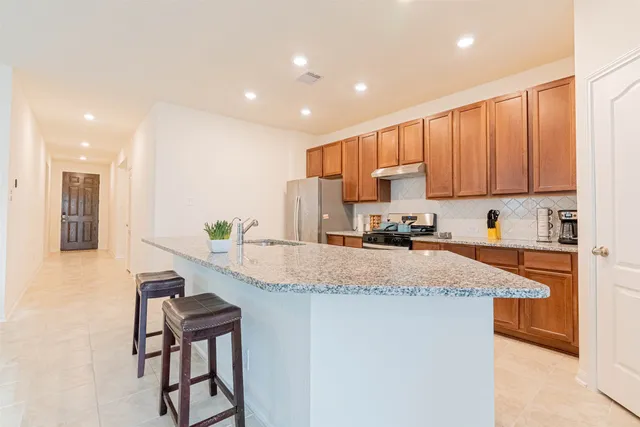 a kitchen with stainless steel appliances granite countertop a refrigerator a stove a sink a dining table and chairs with wooden floor