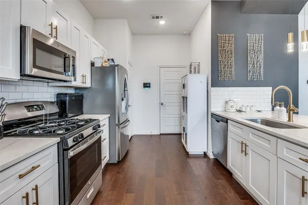 a kitchen with stainless steel appliances a sink dishwasher a refrigerator a stove top oven and wooden floor