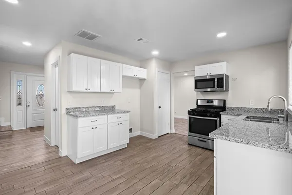 a kitchen with granite countertop a stove top oven a sink dishwasher and a refrigerator with wooden floor