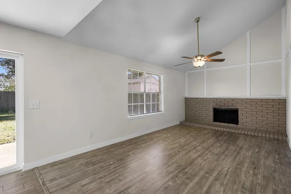 a view of an empty room with wooden floor fireplace and a window