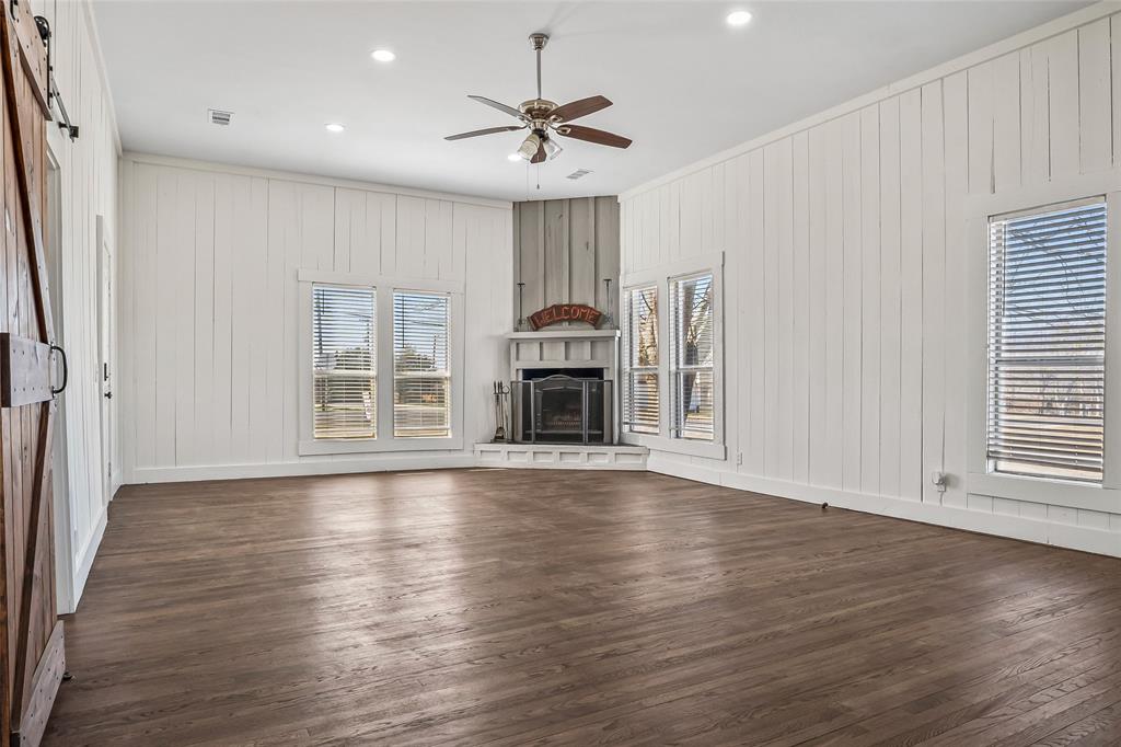 442 West McCart Street Krum, TX 76249 - Photo 8 of 40 an empty room with wooden floor fireplace and windows