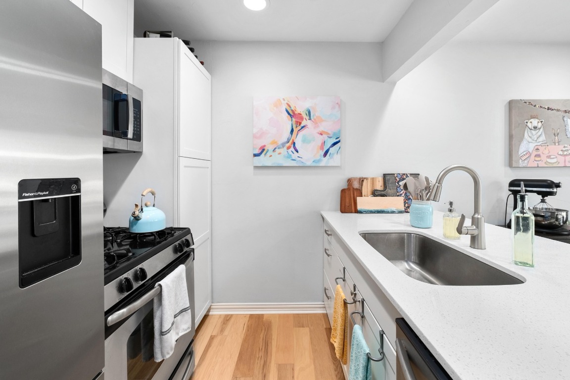 1210 Windsor Road, Unit 122 Austin, TX 78703 - Photo 11 of 24 Kitchen with appliances with stainless steel finishes, white cabinetry, light stone countertops, and light wood-style flooring