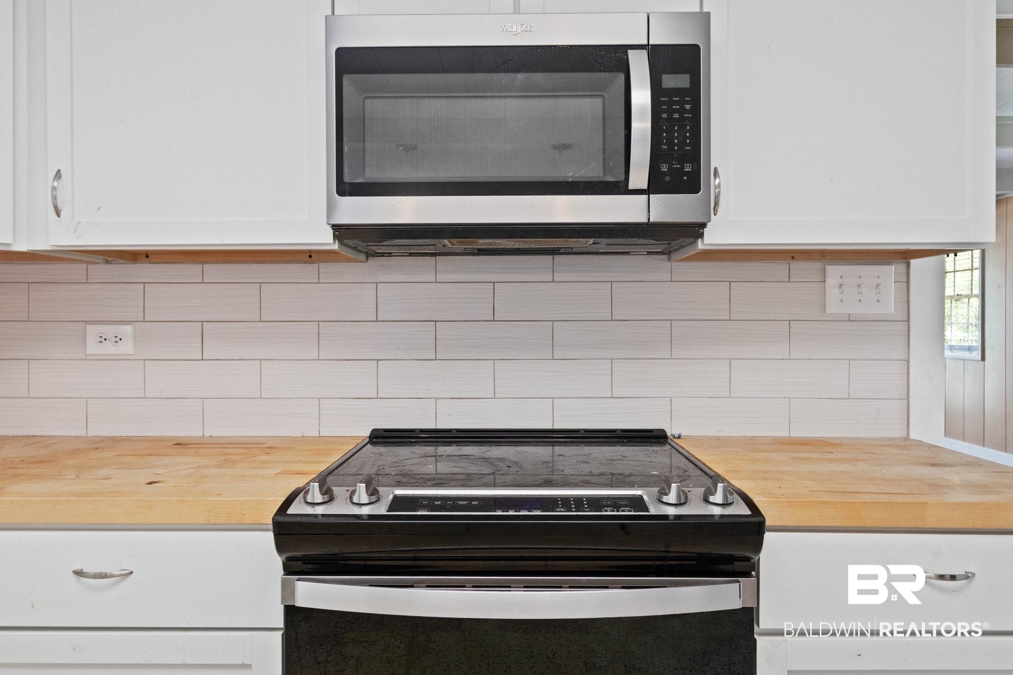 384 Old Bratt Road Atmore, AL 36502 - Photo 20 of 64 Kitchen featuring a stainless steel range with a black cooktop, an over-the-range stainless steel microwave, white shaker-style cabinetry, a subway tile backsplash, and light wood-finish countertops