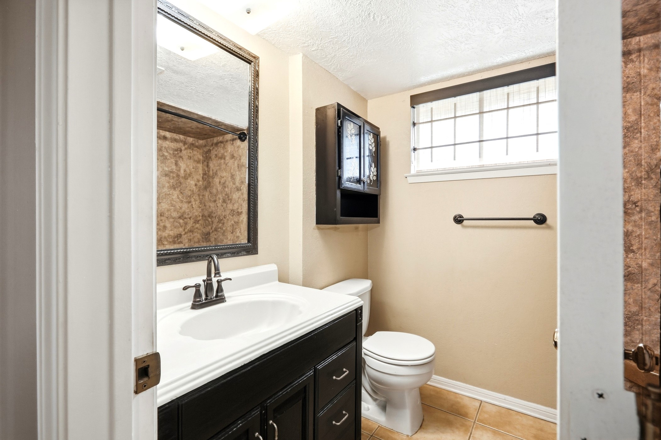 1507 Willow Rock Road Houston, TX 77088 - Photo 26 of 27 Updated full bath with a dark wood vanity, framed mirror, wall storage cabinet, tile flooring, and a high window for light and privacy.