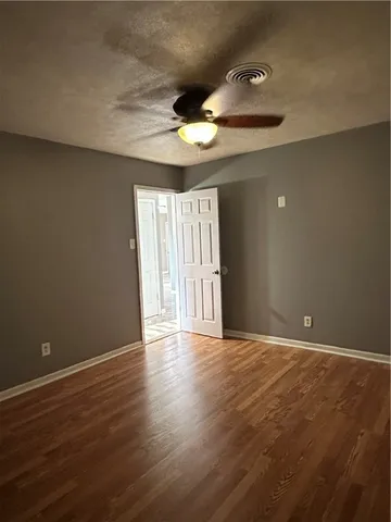 a view of an empty room with wooden floor and a ceiling fan