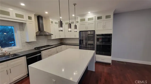 a kitchen with stainless steel appliances a stove a refrigerator a sink and white cabinets with wooden floor