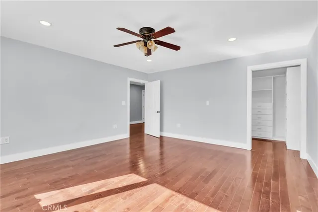 a view of an empty room with wooden floor and a ceiling fan