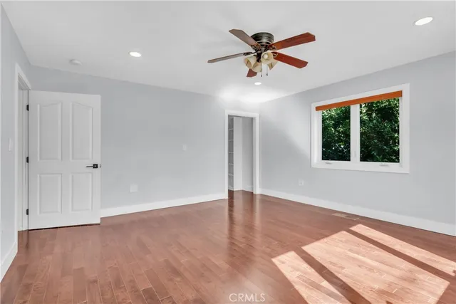 an empty room with wooden floor fan and windows