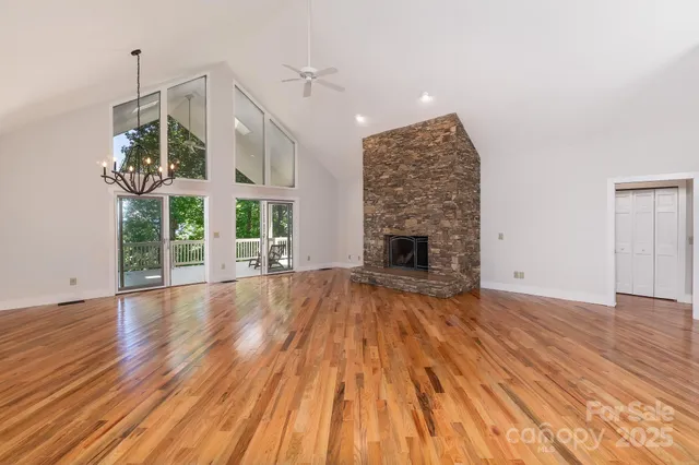 an empty room with wooden floor fireplace chandelier and windows