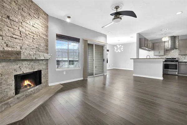 a view of an empty room and kitchen with fireplace wooden floor